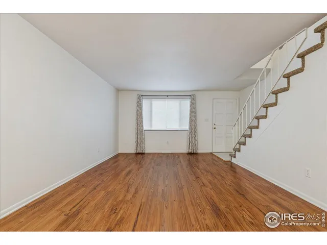 a view of an empty room with wooden floor and stairs