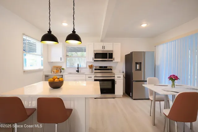 a kitchen with stainless steel appliances a stove a refrigerator a sink a dining table and chairs