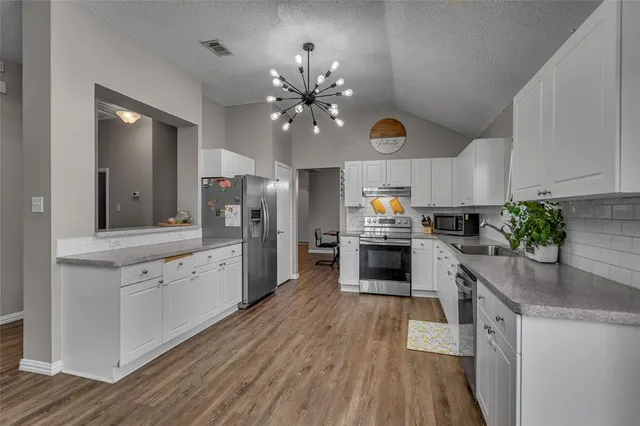 a kitchen with granite countertop a refrigerator a stove a sink dishwasher and white cabinets with wooden floor