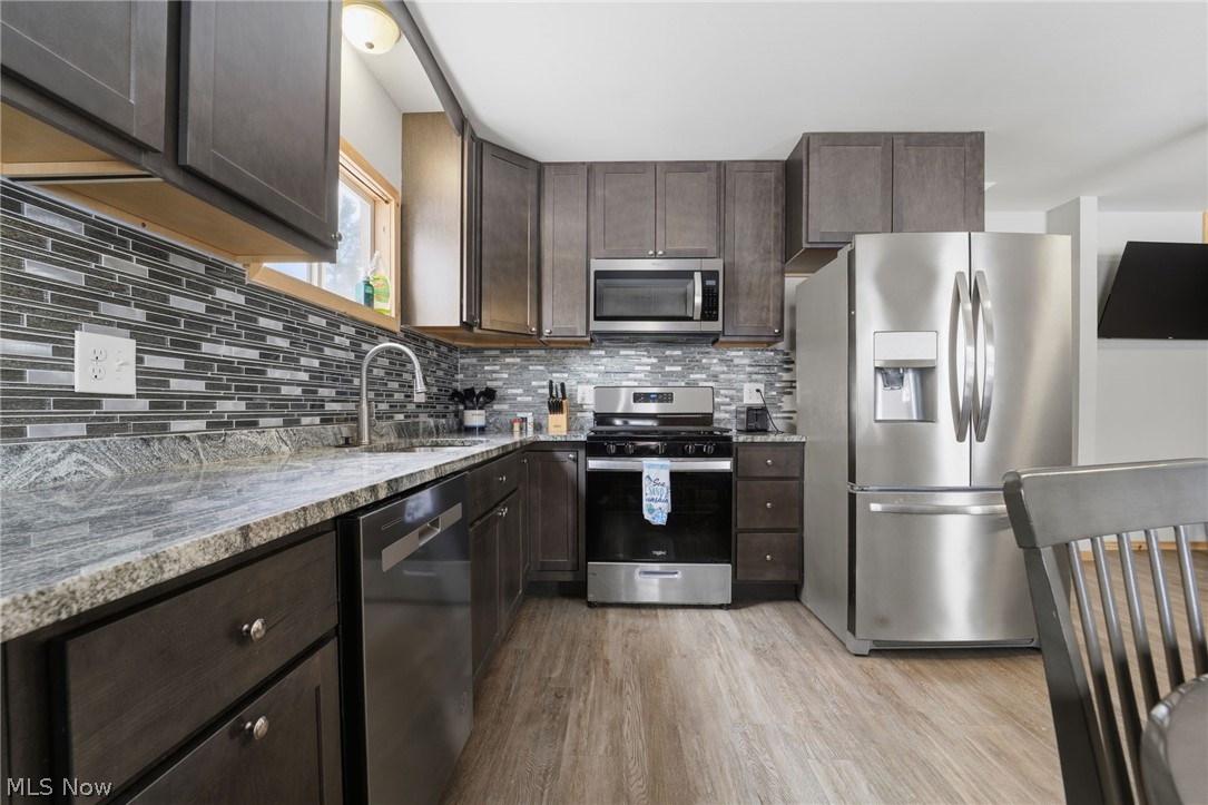 5919 Lake Road West, Unit 33 Ashtabula, OH 44004 - Photo 7 of 22 Kitchen with dark wood finish cabinetry, stainless steel appliances, light stone counters, light wood-type flooring, and decorative backsplash