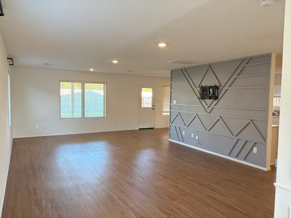 an empty room with wooden floor entryway and windows