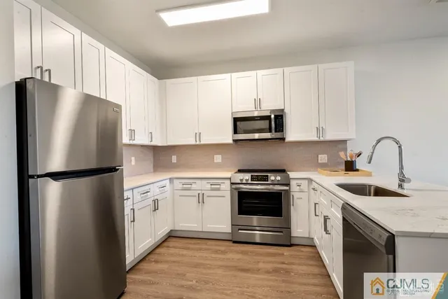 a kitchen with stainless steel appliances granite countertop a stove a sink a refrigerator white cabinets and wooden floor