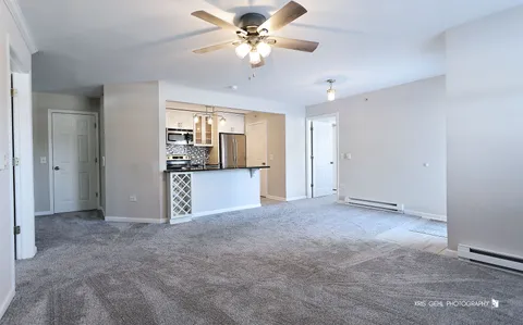 an empty room with chandelier fan and kitchen view