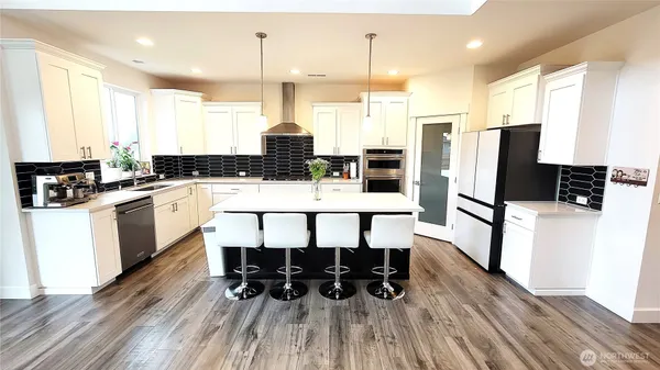 a kitchen with stainless steel appliances kitchen island granite countertop a stove a refrigerator a sink and white cabinets with wooden floor