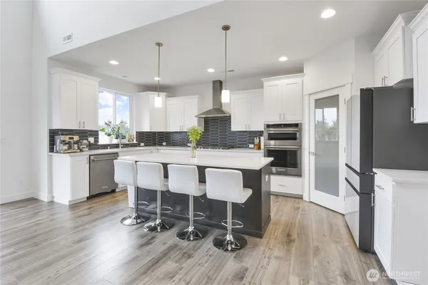 a kitchen with kitchen island granite countertop a refrigerator a stove a sink a dining table and chairs with wooden floor