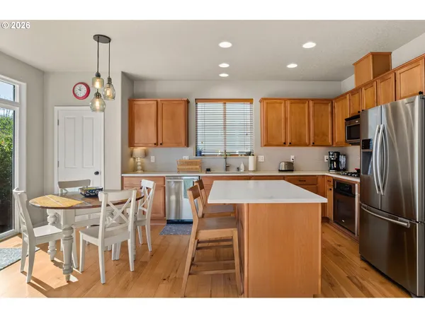 a kitchen with stainless steel appliances kitchen island granite countertop a refrigerator a stove a sink dishwasher with a dining table and chairs with wooden floor