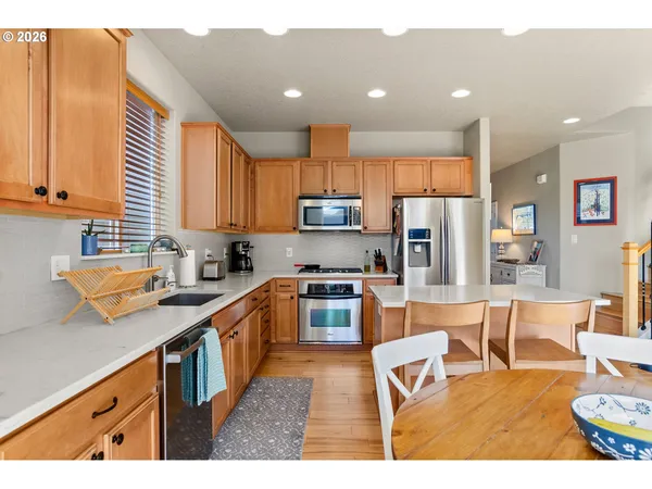 a kitchen with stainless steel appliances granite countertop a stove top oven a sink dishwasher a dining table and chairs with wooden floor