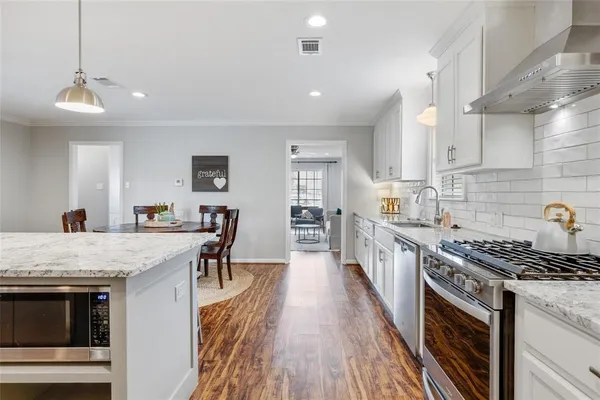 a kitchen with stainless steel appliances granite countertop a stove top oven a sink dishwasher and a refrigerator with wooden floor