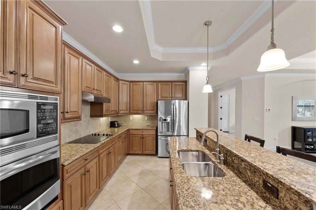 9254 Veneto Place Naples, FL 34113 - Photo 7 of 30 Kitchen with stainless steel appliances, a raised ceiling, light stone counters, hanging light fixtures, and sink