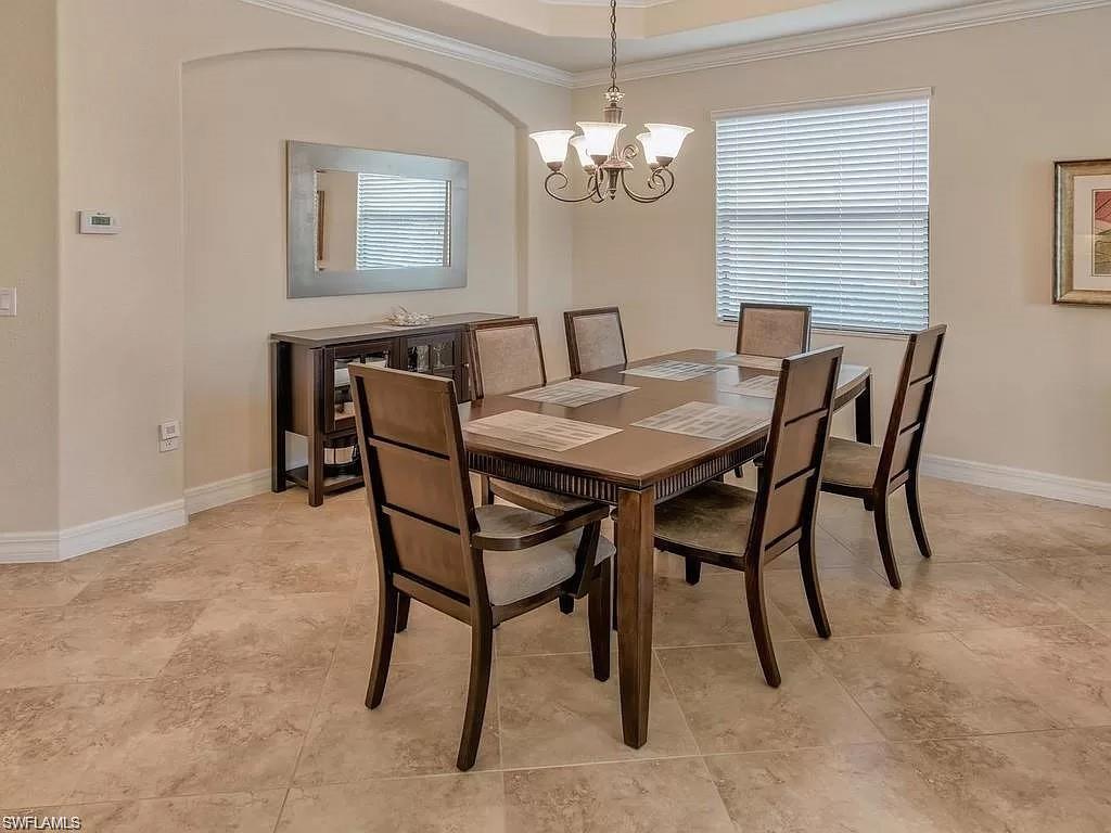 9254 Veneto Place Naples, FL 34113 - Photo 8 of 30 Dining area featuring light tile patterned flooring, a notable chandelier, ornamental molding, and a tray ceiling
