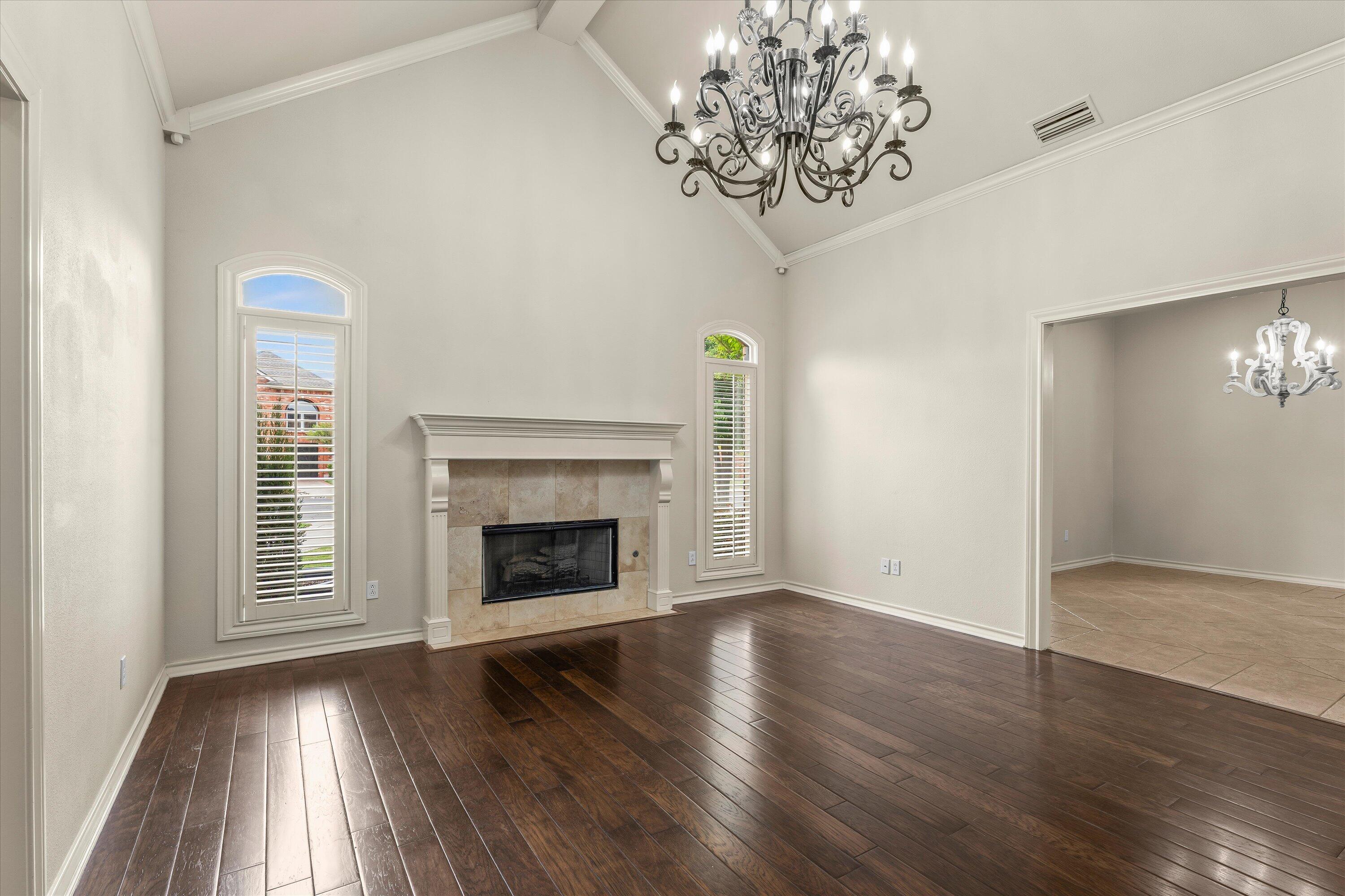 5110 96th Street Lubbock, TX 79424 - Photo 16 of 50 an empty room with wooden floor a chandelier fan a fireplace and windows