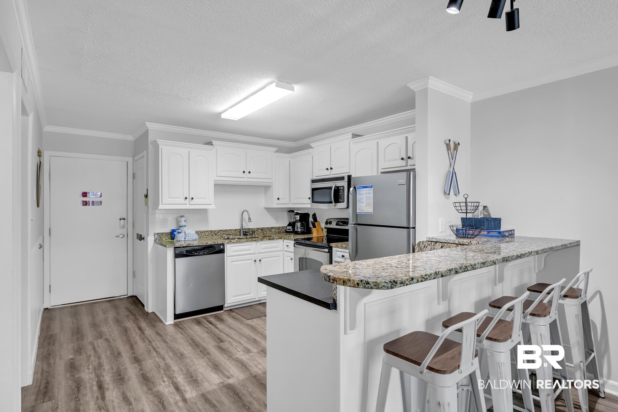 400 Plantation Road, Unit 2118 Gulf Shores, AL 36542 - Photo 6 of 59 Open-concept kitchen featuring white cabinetry, granite countertops, stainless steel appliances, wood-finish flooring, and a breakfast bar with seating