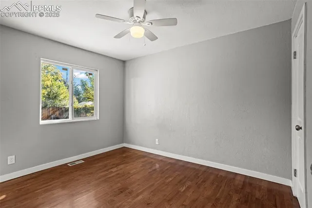 an empty room with wooden floor chandelier fan and windows