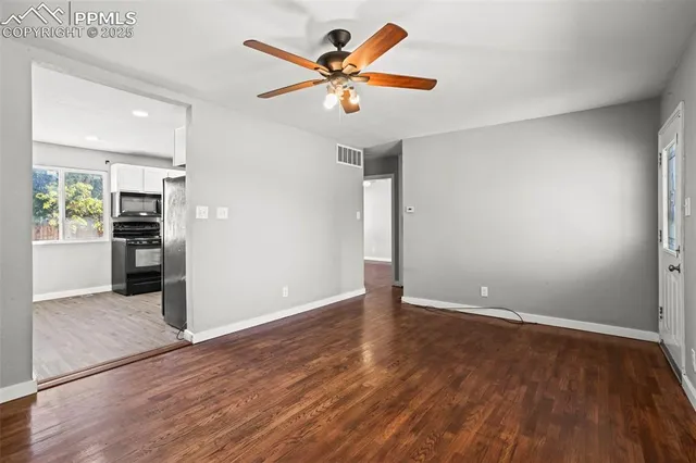 an empty room with wooden floor and a ceiling fan