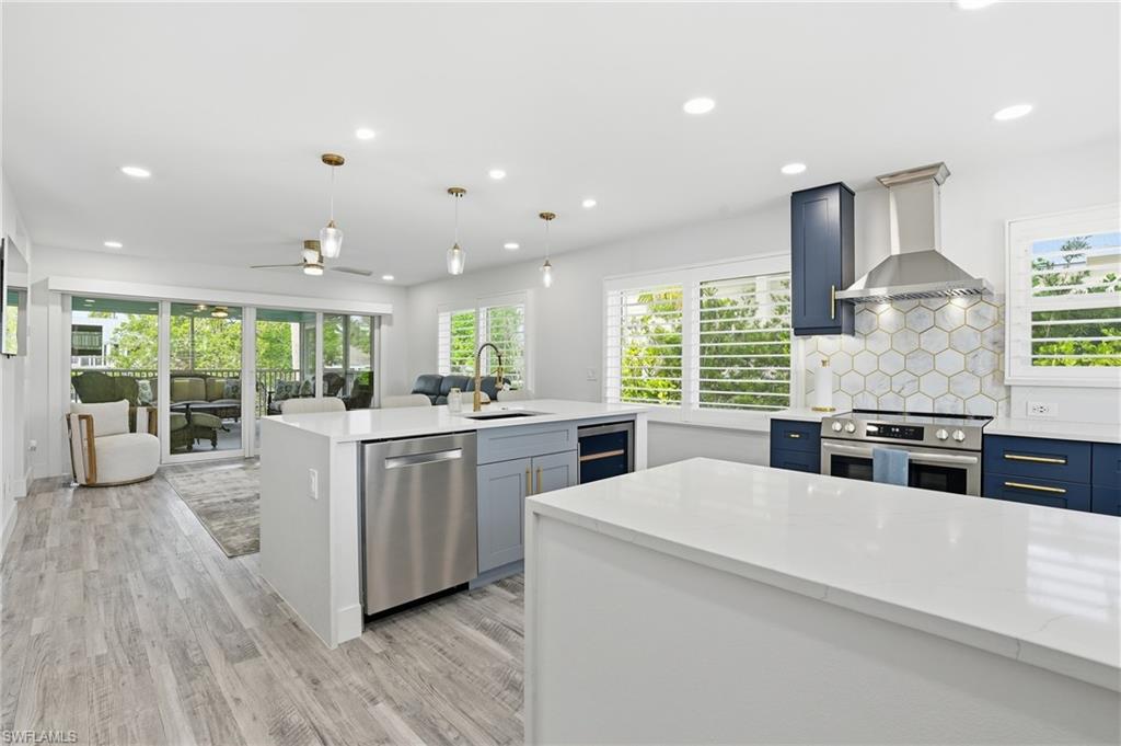 270 Dundee Road Fort Myers Beach, FL 33931 - Photo 12 of 48 Kitchen with ceiling fan, light stone counters, decorative light fixtures, stainless steel appliances, and a center island with sink - Virtually Edited Image