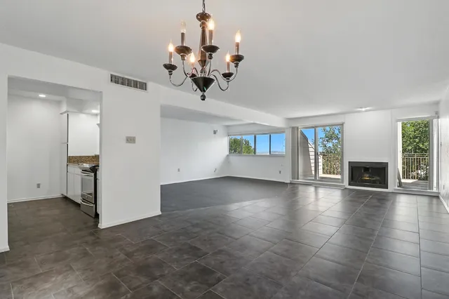 a view of a livingroom with a fireplace a chandelier wooden floor and windows