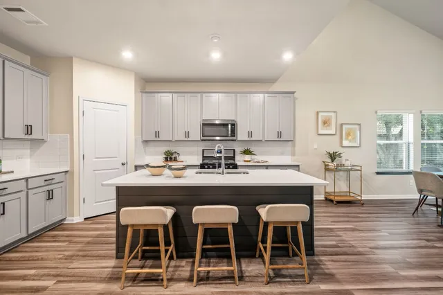 a kitchen with stainless steel appliances granite countertop a stove top oven a sink dishwasher a refrigerator and white cabinets with wooden floor
