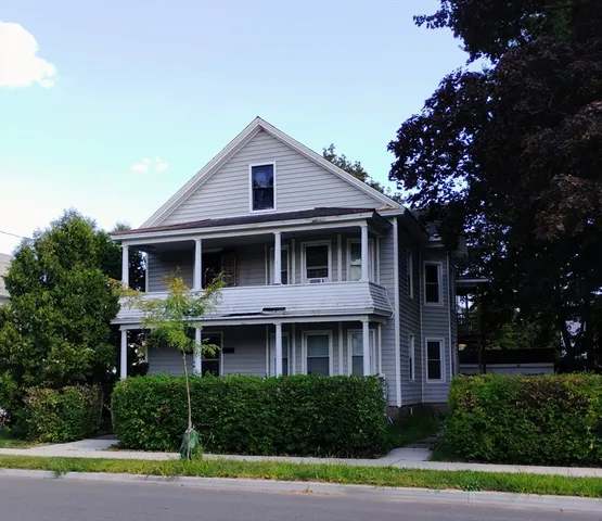a view of a brick house with a yard plants and large tree