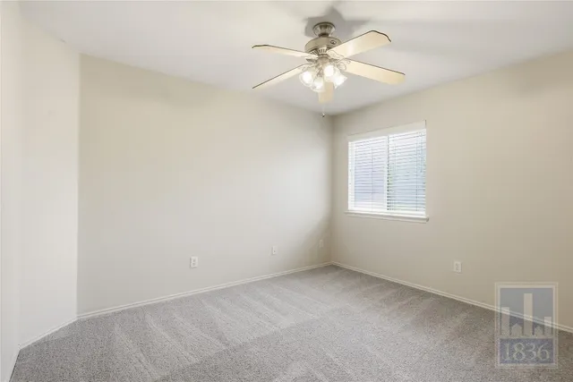 an empty room with a chandelier fan and windows