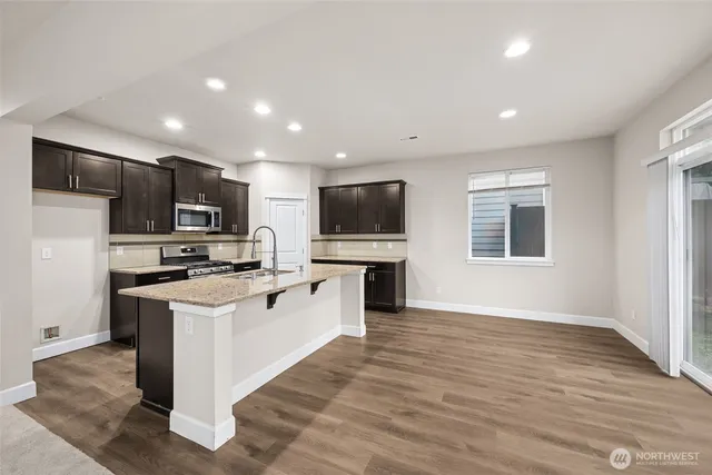 a kitchen with stainless steel appliances kitchen island granite countertop a stove top oven a sink dishwasher a refrigerator and a refrigerator with wooden floor