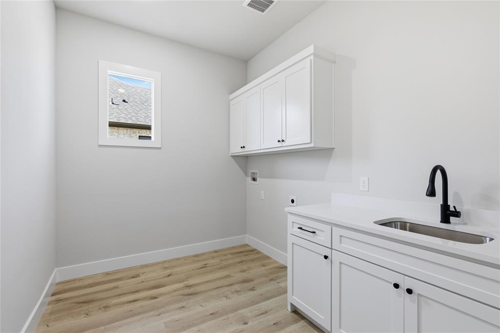 713 Anne Road Van Alstyne, TX 75495 - Photo 23 of 29 Utility space featuring white cabinetry, a single basin sink with a black gooseneck faucet, light wood-finish flooring, and a window