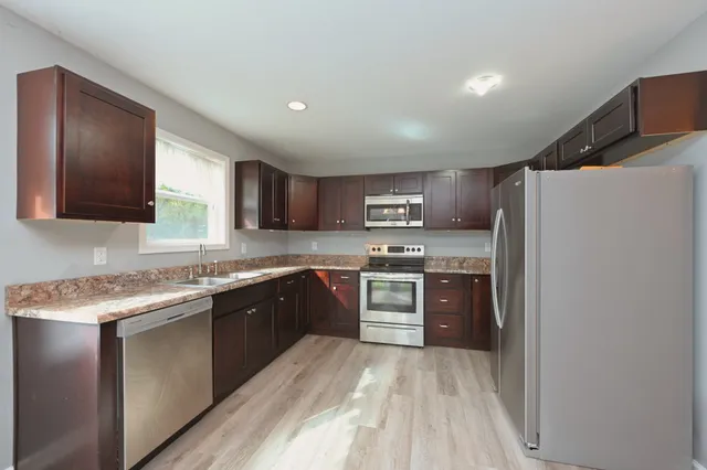 a kitchen with stainless steel appliances granite countertop a refrigerator a sink dishwasher a oven with white cabinets and wooden floor