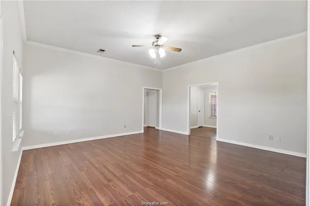 a view of an empty room with wooden floor and a ceiling fan