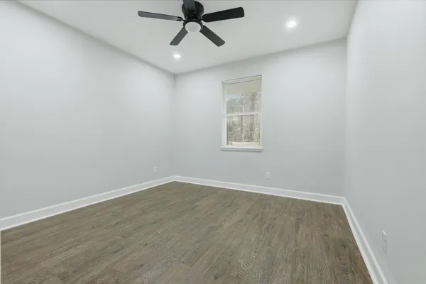an empty room with wooden floor ceiling fan and windows