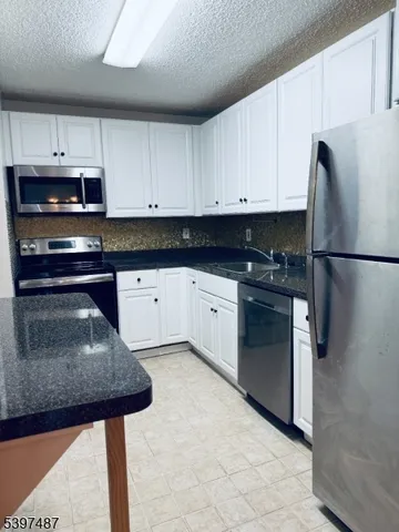a kitchen with granite countertop a sink stainless steel appliances and white cabinets