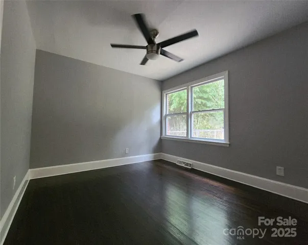 an empty room with wooden floor fan and windows