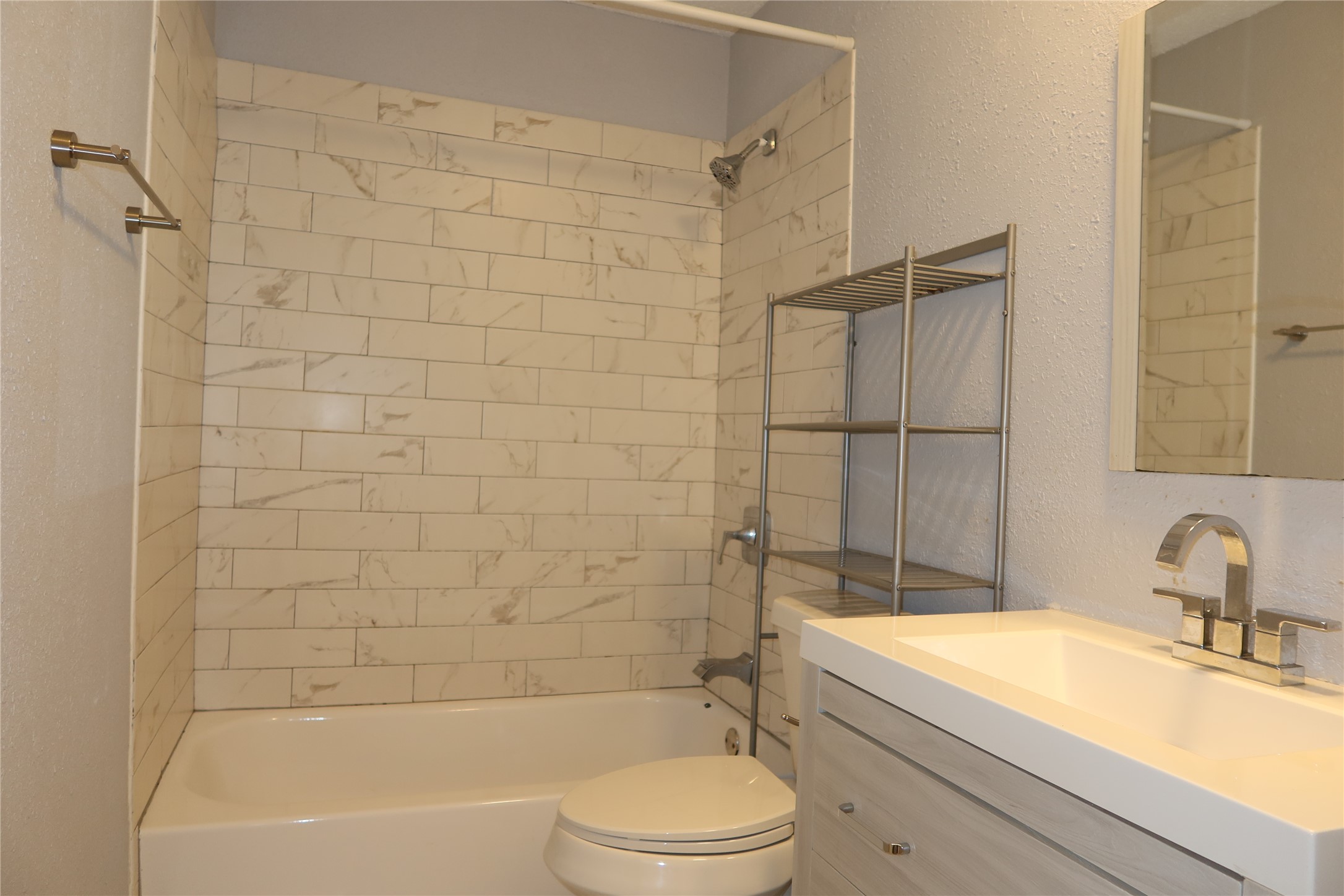6914 Rifle Bend, Unit A Austin, TX 78736 - Photo 21 of 25 Tiled shower walls surround the bathtub next to a modern single-sink vanity.