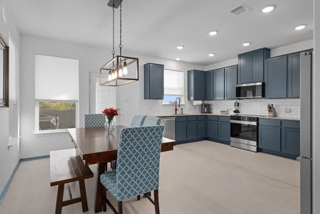 a kitchen with kitchen island a dining table chairs stainless steel appliances and windows