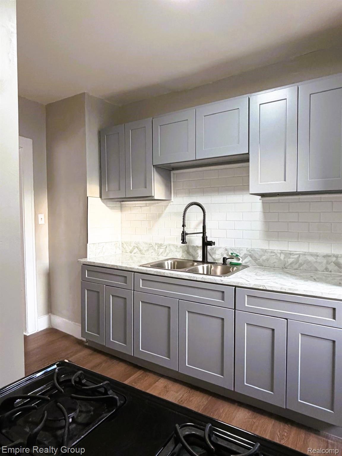 6441 Appoline Street, Unit 1 Dearborn, MI 48126 - Photo 9 of 13 Kitchen featuring gray cabinetry, dark wood-type flooring, black gas stovetop, light stone countertops, and backsplash