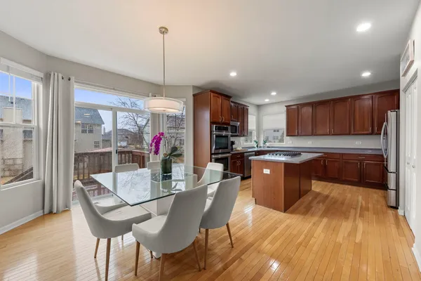 a kitchen with stainless steel appliances granite countertop a refrigerator a sink dishwasher a dining table and chairs with wooden floor