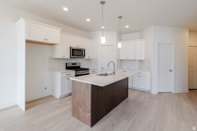 4748 Heartwood Road, Unit 434 Mapleton, UT 84664 - Photo 9 of 18 Kitchen featuring stainless steel appliances, a kitchen island with sink, light wood-type flooring, light stone countertops, and two tone color scheme