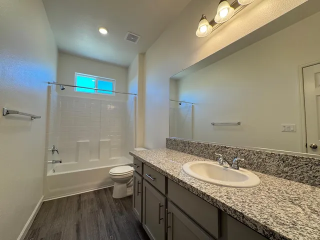 a bathroom with a granite countertop sink a toilet a shower and a mirror