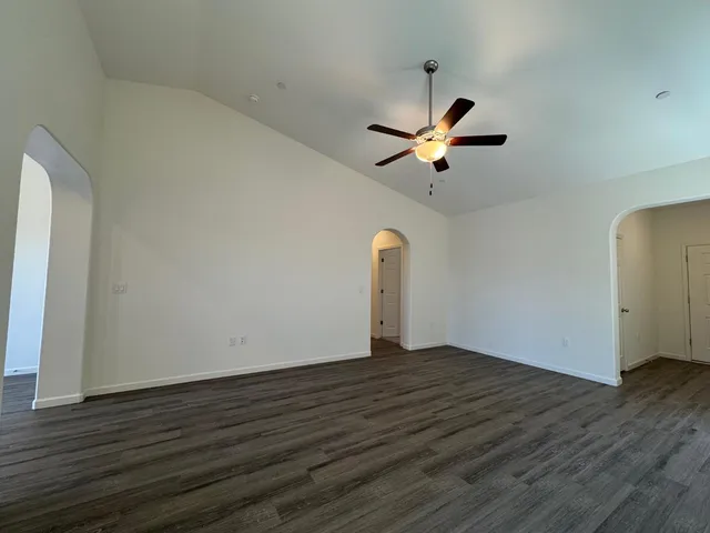 a view of an empty room and chandelier fan and wooden floor