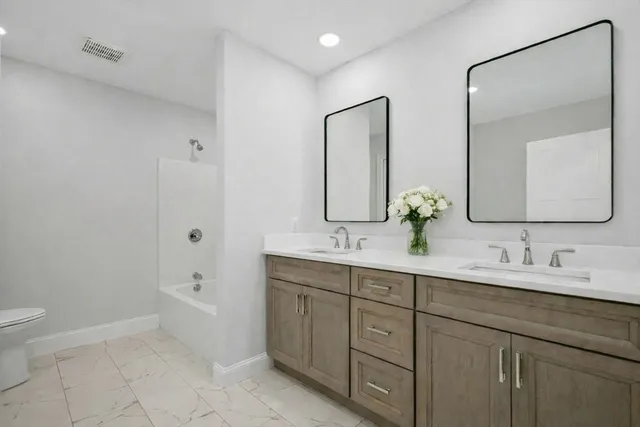 a bathroom with a double vanity sink toilet mirror and bathtub