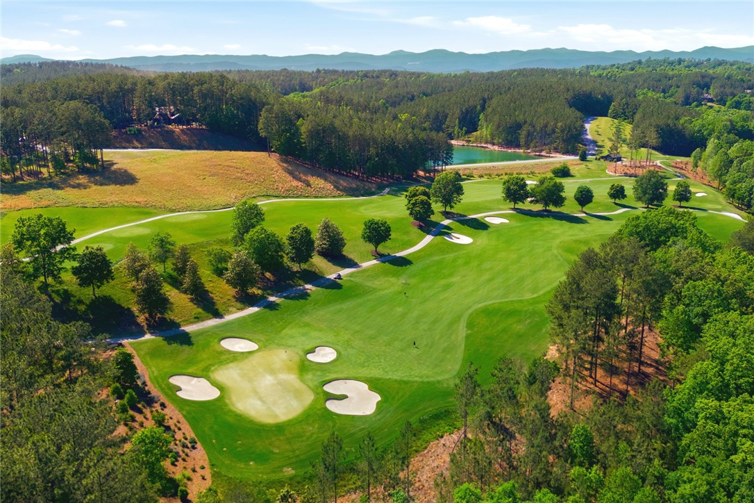 130 River Ridge Road Sunset, SC 29685 - Photo 47 of 47 An aerial perspective reveals the lush, well-maintained greens and sand traps of a scenic golf course, framed by extensive wooded areas and distant mountains.