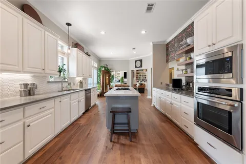 a large kitchen with stainless steel appliances granite countertop a stove a sink dishwasher and a microwave oven with wooden floor