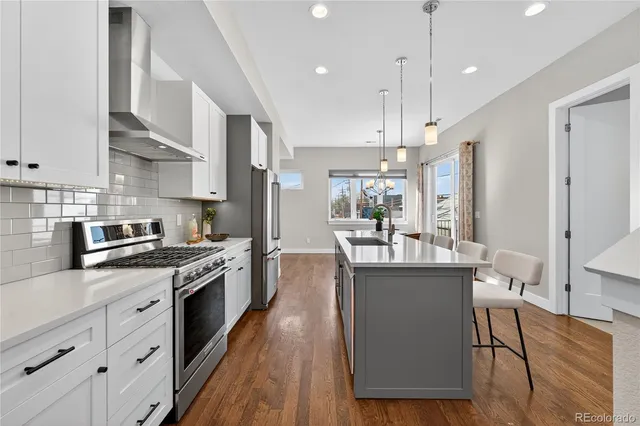 a kitchen with stainless steel appliances granite countertop a stove a sink dishwasher a refrigerator white cabinets and wooden floor next to a window