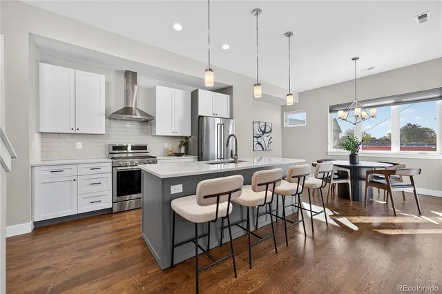 a kitchen with stainless steel appliances granite countertop a stove a refrigerator a kitchen island a dining table and chairs with wooden floor