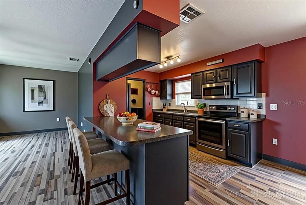 11327 Grove Street Leesburg, FL 34788 - Photo 13 of 40 a kitchen with stainless steel appliances granite countertop a stove top oven a sink dishwasher a dining table and chairs with wooden floor