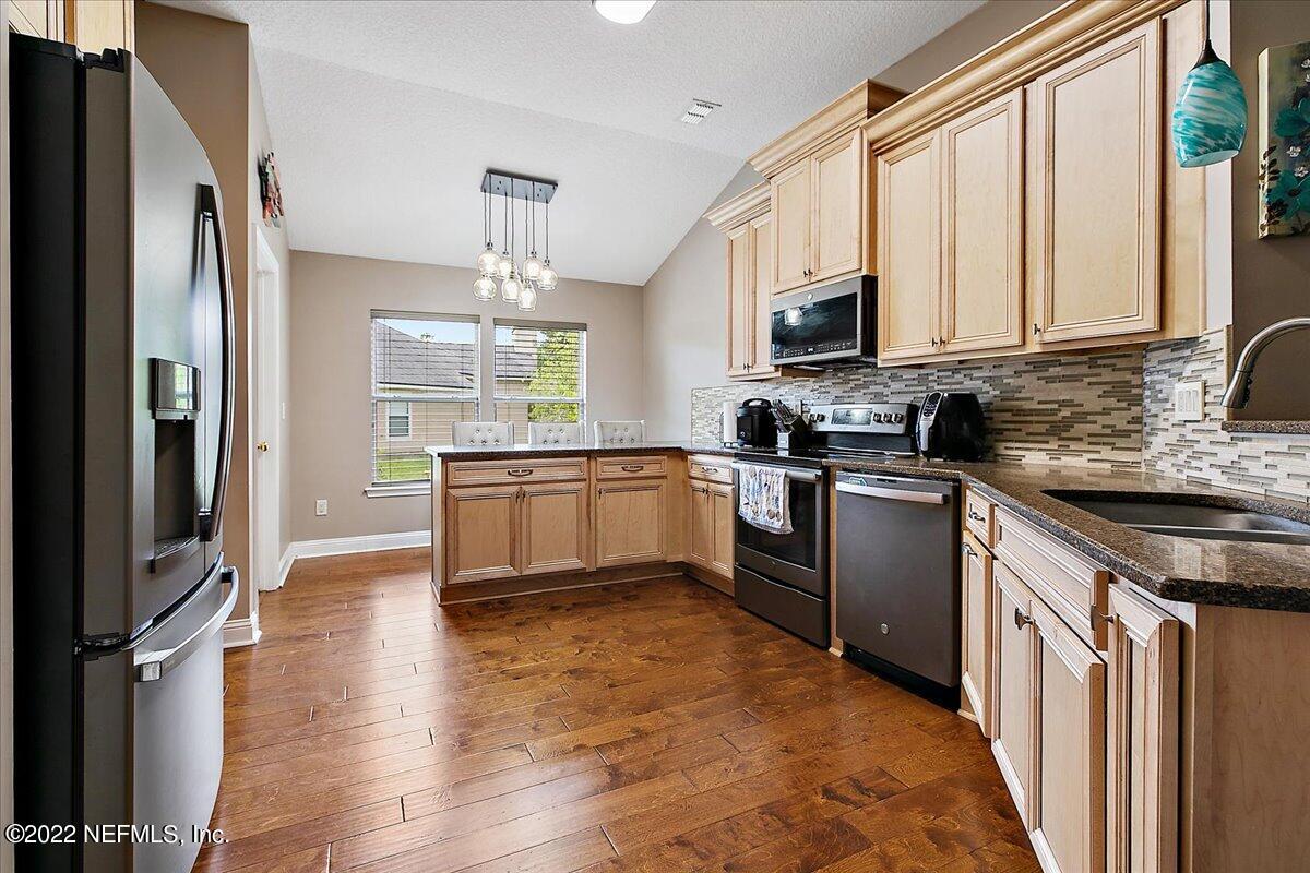 86003 Maple Leaf Place Yulee, FL 32097 - Photo 6 of 27 a kitchen with stainless steel appliances granite countertop a refrigerator a sink dishwasher a stove with wooden cabinets and floor