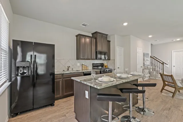 a kitchen with stainless steel appliances kitchen island granite countertop a refrigerator a sink a stove and chairs with wooden floor