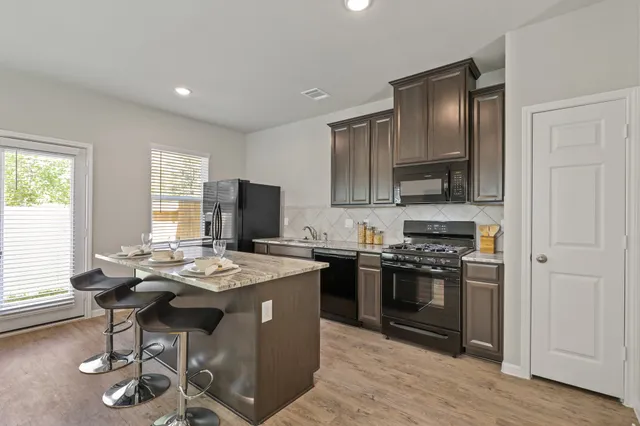 a kitchen with stainless steel appliances kitchen island granite countertop a stove a sink dishwasher and a refrigerator with wooden floor