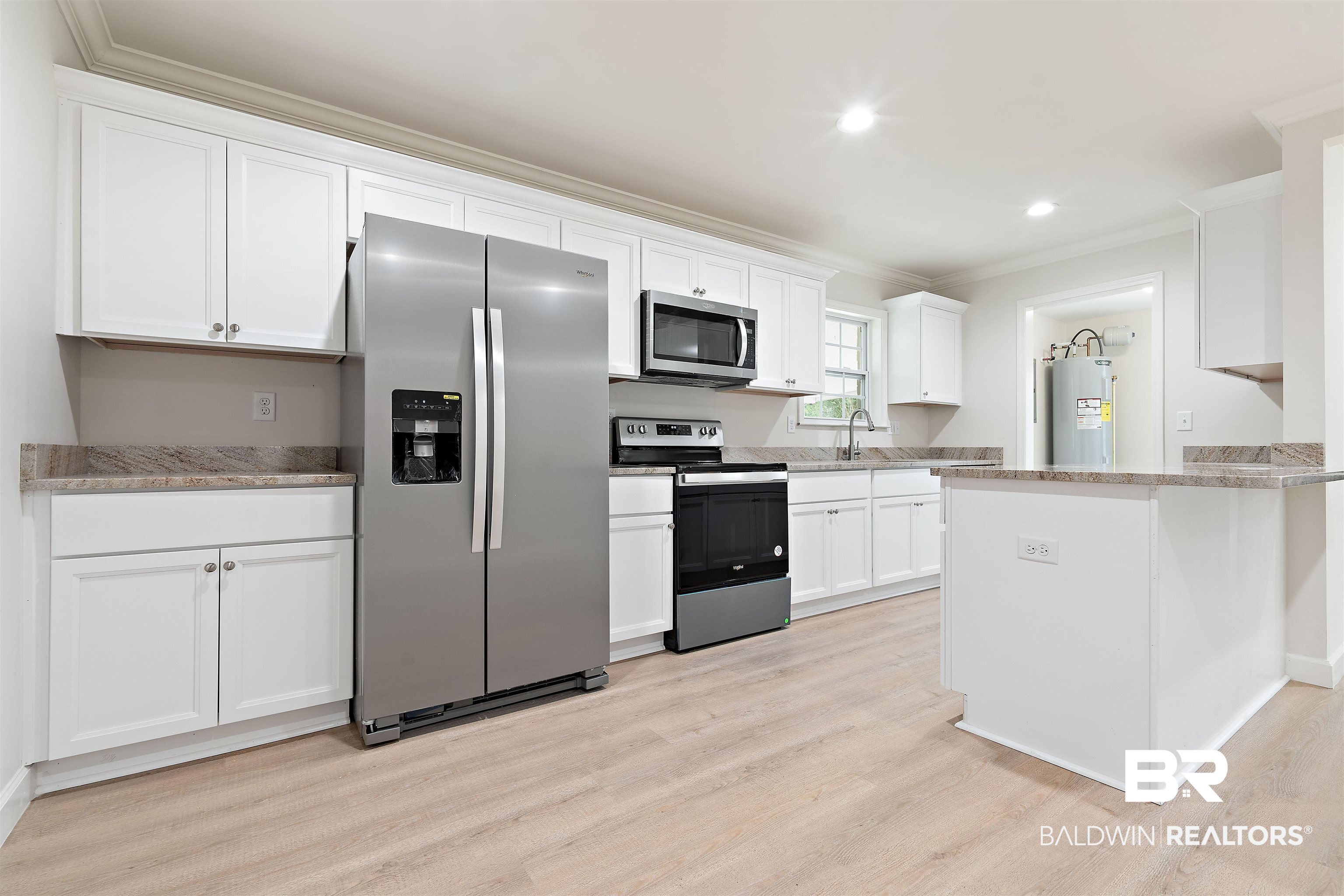 1315 Johnson Road Daphne, AL 36526 - Photo 11 of 41 Kitchen with electric water heater, appliances with stainless steel finishes, light hardwood / wood-style floors, white cabinetry, and ornamental molding
