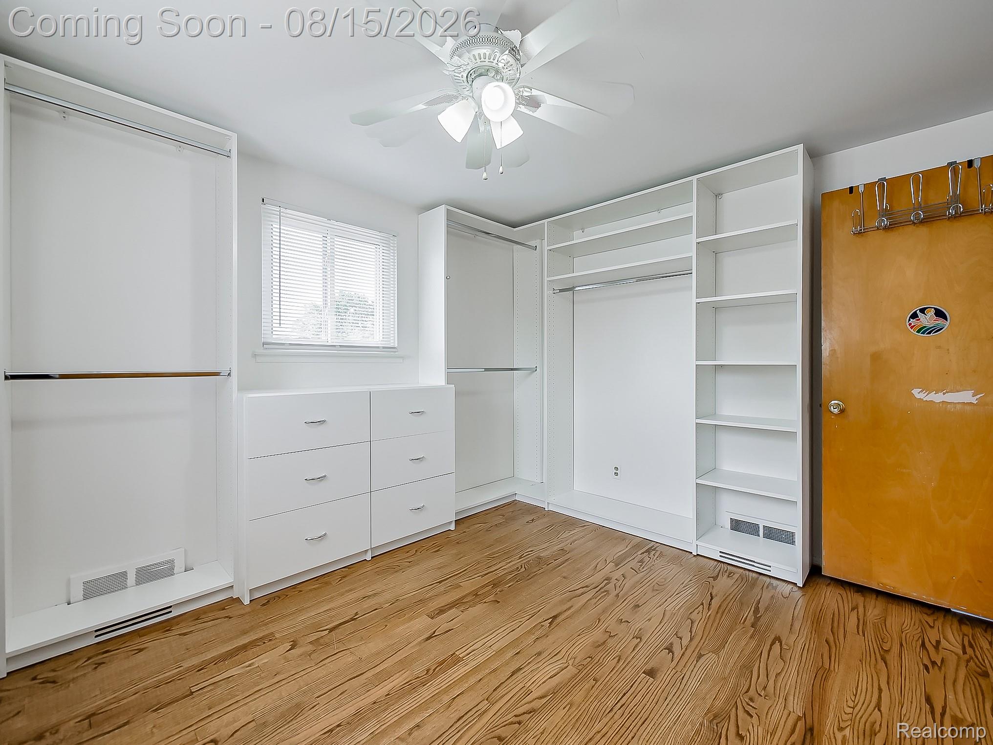 21131 Harvard Road Southfield, MI 48076 - Photo 14 of 33 Wood-finish flooring, built-in white shelving, integrated white drawers, a ceiling fan, and a window with blinds