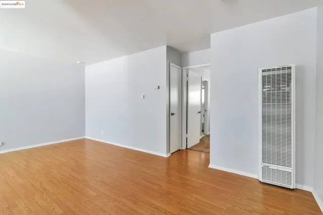 a view of an empty room with wooden floor and a bathroom