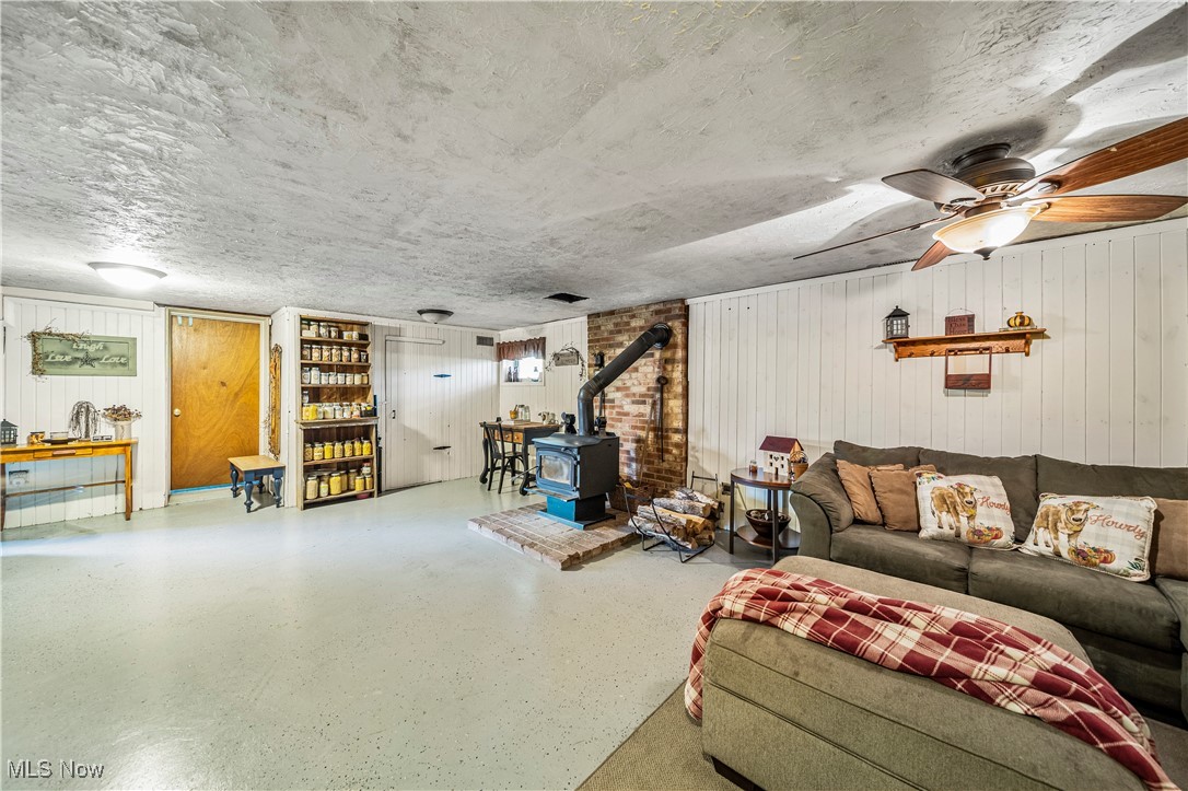 6981 Howard Road Williamsfield, OH 44093 - Photo 29 of 42 Living room featuring a textured ceiling, ceiling fan, wooden walls, and a wood stove